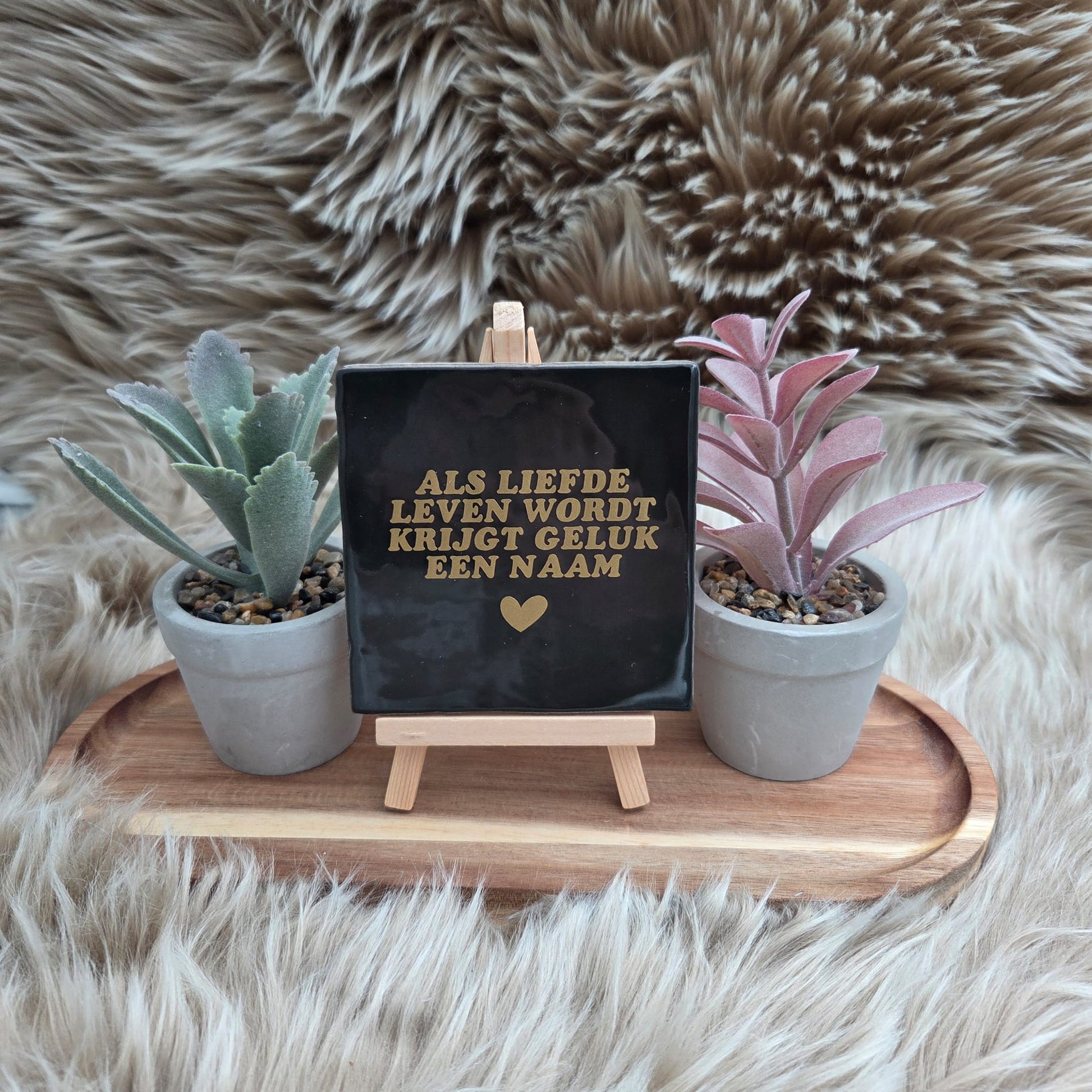 Keramisch zwart tegeltje met gouden tekst “Als liefde leven wordt krijgt geluk een naam” op houten standaard met twee plantjes – decoratie of cadeau.